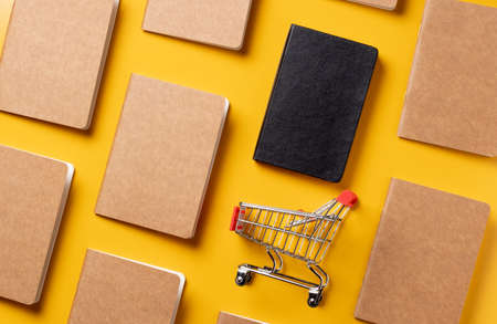 content marketing concept,top view Black and Kraft paper book alignment in pattern with shopping cart on yellow desk surface.leave space for display your contentの写真素材