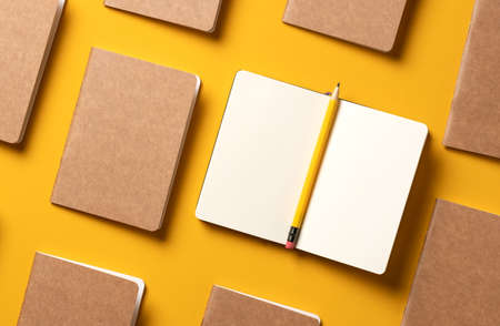 content marketing concept,.top view of hand writing on open notebook and yellow pencil align with kraft paper book in pattern on yellow table background.mockup for advertise content onlineの写真素材