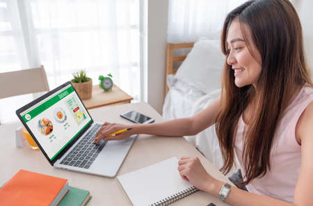 Asian woman order grocery online with laptop at home.new normal digital lifestyle with technology shopping onlneの写真素材