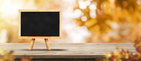 Autumn background.Blank blackboard on rustic wood table with blur forest tree with sunlight,Autumn fall backdrop, banner for product display for advertise on online,thanksgiving conceptの写真素材