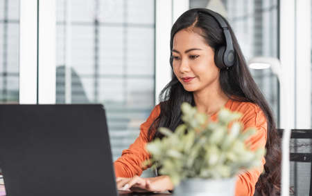 Asian woman as content creator typing on laptop listening podcast while working from home.new normal lifestyle using technologyの写真素材