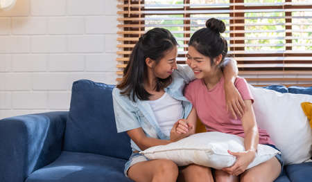 Happy asian lesbian couple holding hand and hug together at sofa in living room at cozy homeの写真素材
