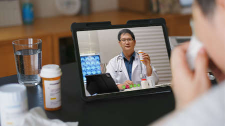 Telehealth concept,asian woman video call with her doctor about  fever illness while staying at home. Close up of patient about illness in video conferencing with general practitioner on digital tablet.の写真素材