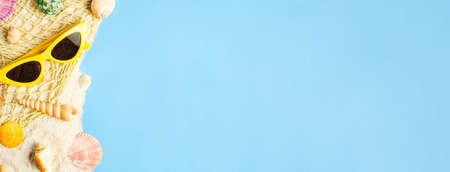 Tropical summer beach sea accessories objects,sunglasses,white net,sailing and seashell on white sand  over pastel blue background bannerの写真素材