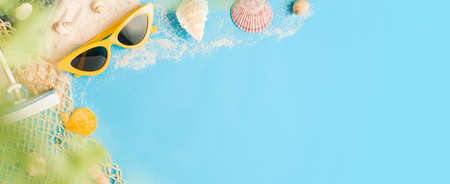 Tropical summer beach sea accessories objects,sunglasses,green straw bag,sailing and seashell over pastel blue background bannerの写真素材