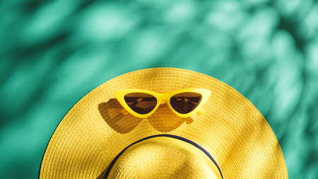 Yellow straw hat and sunglasses over green turquoise background with sunlight and tree shadow ,Minimal summer beach seaの写真素材