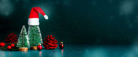 Merry Christmas and happy new year snow falling with xmas tree and red Santa clause hat on dark green background.Banner mockup space for display of product or design or textの写真素材