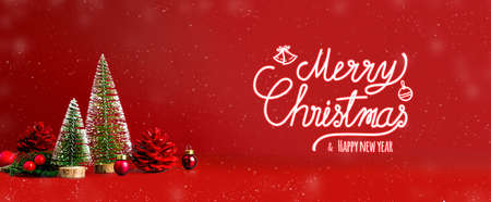 Merry Christmas and happy new year text with snow falling on red background with xmas tree and pine cone on.Winter holiday greeting cardの写真素材