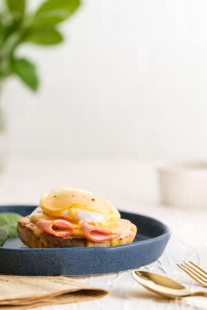 egg Benedict with hollandaise sauce on blue plate on table in white kitchenの写真素材
