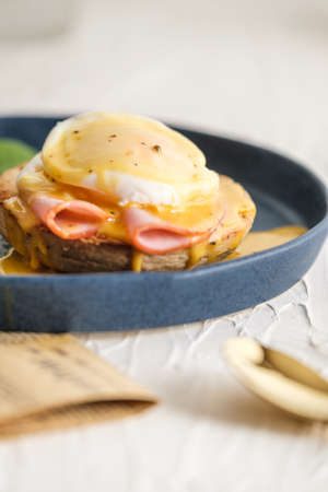 egg Benedict with hollandaise sauce on blue plate on table in white kitchenの写真素材