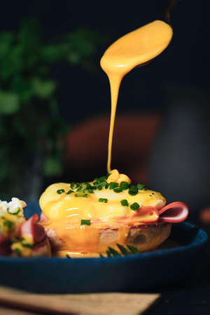 egg Benedict with hollandaise sauce on dark blue plate on table in kitchen
