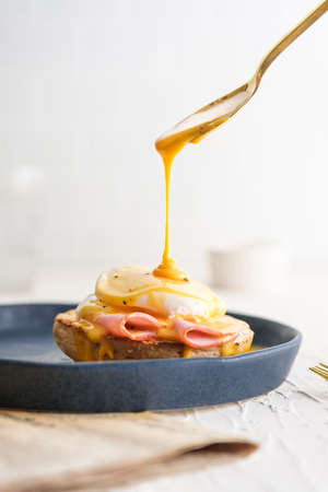 egg Benedict with hollandaise sauce on blue plate on table in white kitchenの写真素材