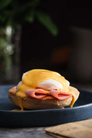 egg Benedict with hollandaise sauce on dark blue plate on table in kitchenの写真素材