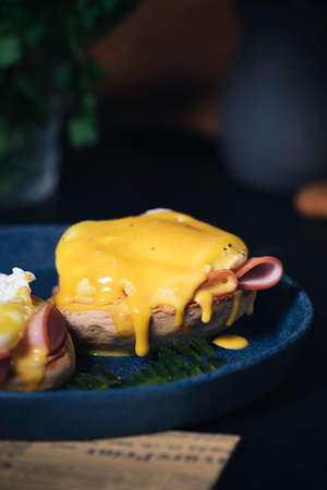 egg Benedict with hollandaise sauce on dark blue plate on table in kitchenの写真素材