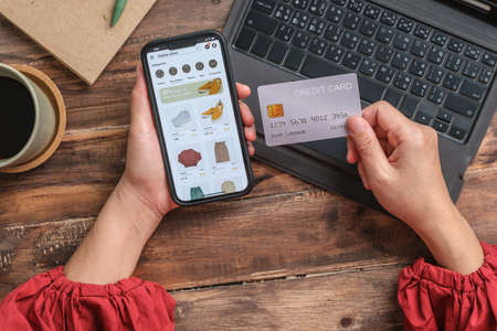 close up woman hand using credit card shopping online on mobile app on wood table at homeの写真素材