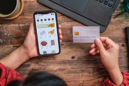 close up woman hand using credit card shopping online on mobile app on wood table at homeの写真素材