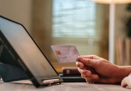 close up woman hand using credit card shopping online on mobile app on wood table at home