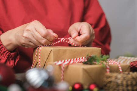 woman making Christmas handmade gift box with brown paper warpping with xmas decor on wood table