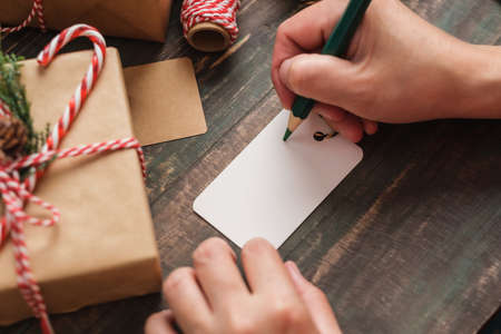 woman writing gift tag and attach to christmas present on wood tableの写真素材