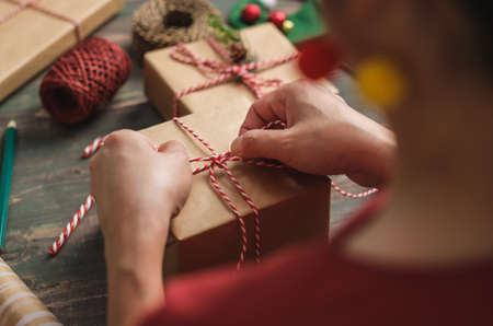 woman making Christmas handmade gift box with brown paper warpping with xmas decor on wood tableの写真素材