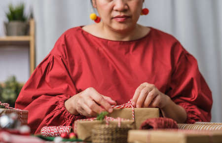woman making Christmas handmade gift box with brown paper warpping with xmas decor on wood tableの写真素材