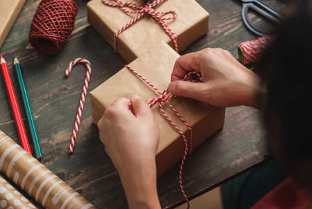 woman making Christmas handmade gift box with brown paper warpping with xmas decor on wood tableの写真素材