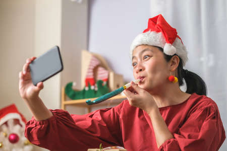 asian woman wear santa hat video call party with friends with mobile phone on table at home