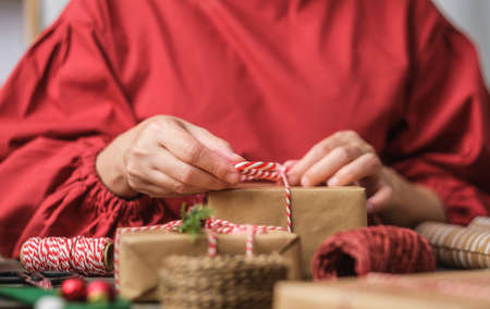 woman making Christmas handmade gift box with brown paper warpping with xmas decor on wood tableの写真素材
