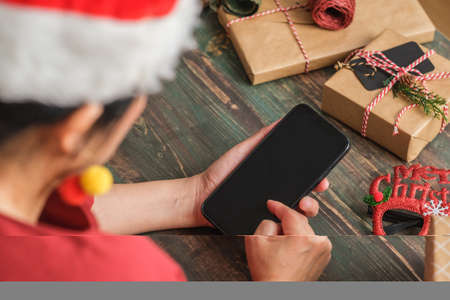 asian woman wear santa hat video call party with friends with mobile phone on table at homeの写真素材