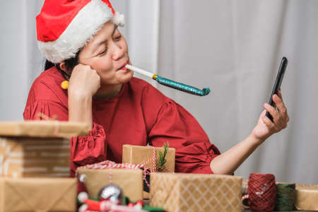 asian woman wear santa hat video call party with friends with mobile phone on table at home