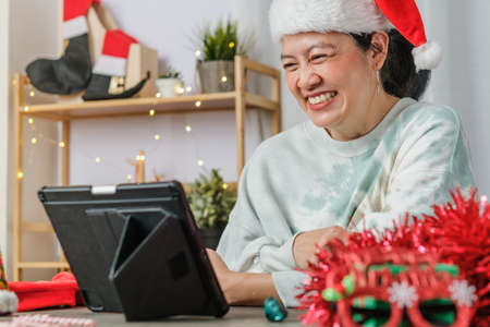 asian woman celebrate new year and christmas party with tablet video call friends at homeの写真素材