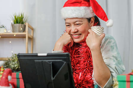 asian woman celebrate new year and christmas party with tablet video call friends at homeの写真素材