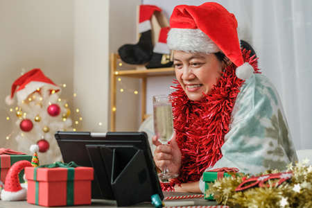 asian woman toasting champagne celebrate new year and Christmas party video call friends at homeの写真素材