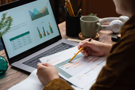 asian woman holding paperwork flow of project checking with laptop data working at homeの写真素材