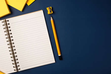 top view open notebook with yellow pencil and notepad on navy blue working tableの写真素材