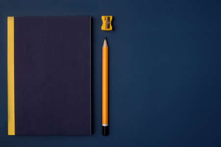 top view cover blue notebook with yellow pencil and notepad on navy blue working tableの写真素材