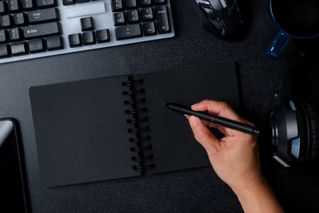 top view hand writing on notebook working on desk with keyboard headphone on black table background