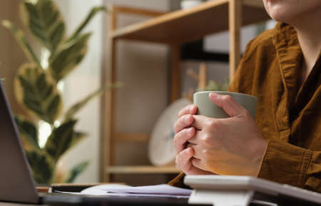 asian woman drink coffee cup and watching live streaming on laptop when work at homeの写真素材