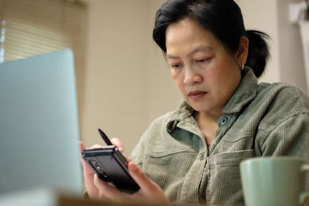 asisn woman use mobile while video conference meeting online with laptop at homeの写真素材