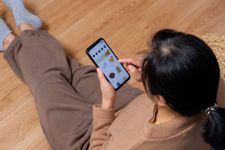 close up hand browsing shopping fashion mobile app on sofa at homeの写真素材