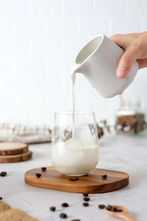 Pour mikl bedore white made Dalgona coffee with fluffy cream served on wood tray.Homemade trendy beverage menu on social mediaの写真素材