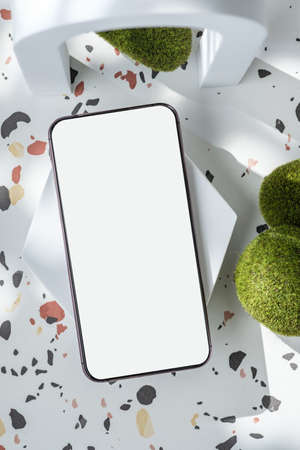 mobile phone on white geometric pedestal on terrazzo background with summer sunlight and moss rockの写真素材