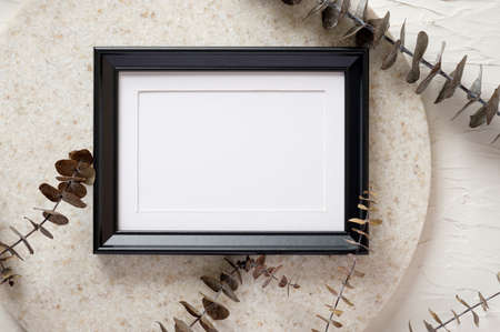 top view blank black photo frame mockup with eucalyptus brancch at peach wallの写真素材
