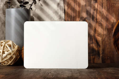 blank paper poster frame with kitchenware on wood table with sunlightの写真素材