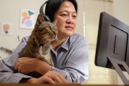 asian woman video conference  with colleague online with tablet and hug her cat at home