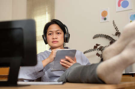 asian woman cross leg on table writing business plan using tablet at homeの写真素材