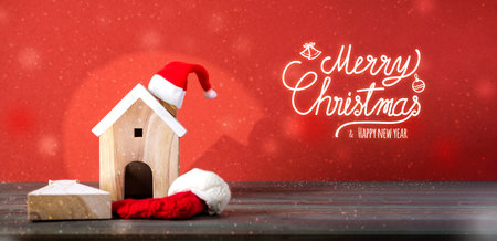 Merry chistmas and happy new year with wooden home wear santa hat on wood table with vivid red backgroundの写真素材