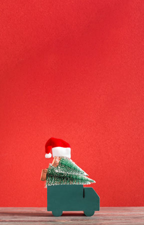 Truck delivery christmas pine tree and santa hat on red background on wood table.Mockup banner with vertical space for design contentの写真素材