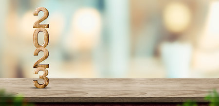 New year 2023 (3d rendering) on brown wood table at blur abstract bokeh light home background with blur leaf foreground,Mock up banner for display of product,holiday celebration grの写真素材