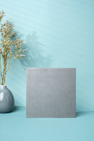 blank poster paper with flower in ceramic vase and window sunlight on pastel blue backgroundの写真素材